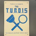 Bewilder Box: Portaclue – The T.U.R.D.I.S - an image of the sign for the turdis. It shows a plunger and magnifying glass crossed over, and the tagline as the crappiest escape room