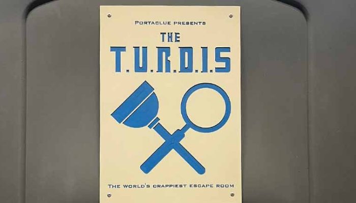 Bewilder Box: Portaclue – The T.U.R.D.I.S - an image of the sign for the turdis. It shows a plunger and magnifying glass crossed over, and the tagline as the crappiest escape room